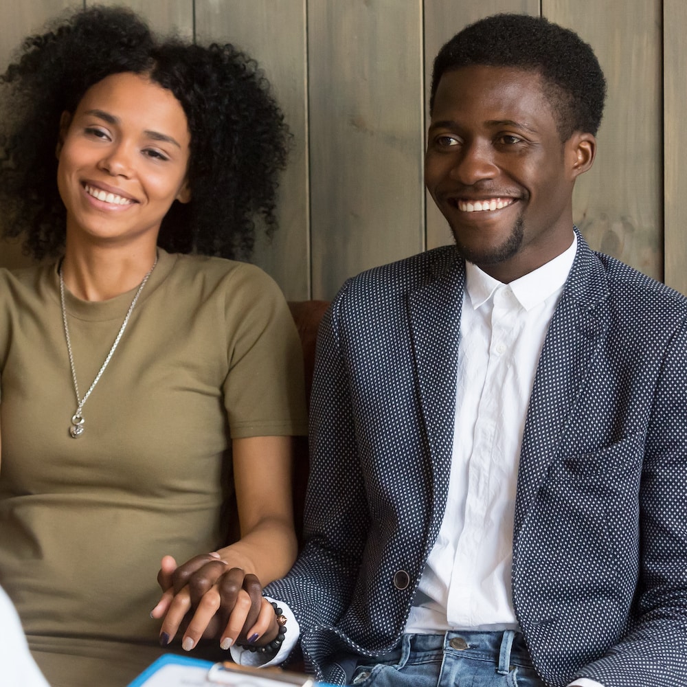 African american young couple holding hands happy to hear good news from doctor, black husband and wife feel relieved after reconciliation during therapy session listening to family marriage counsel