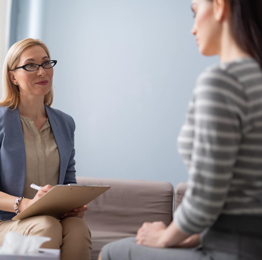 Close up of psychology consultation in clinic. Brunette lady telling about traumatic events to a doctor indoors. Stress concept. Focus on coach